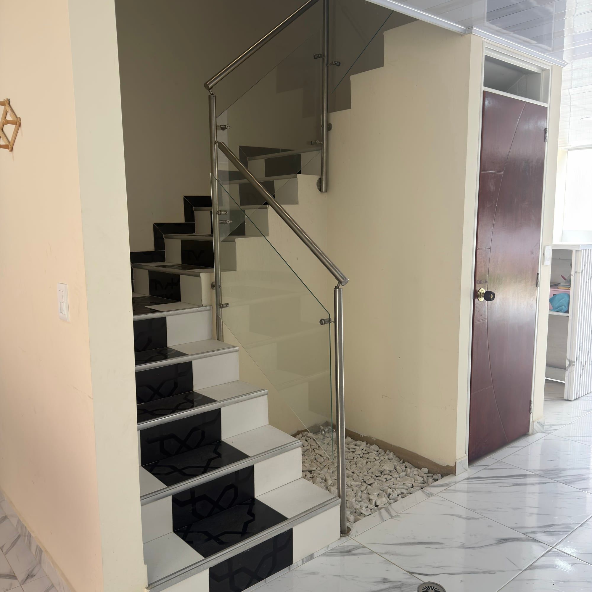 Escalera de peldaños blancos y negros con baranda de vidrio, junto a una puerta de madera.